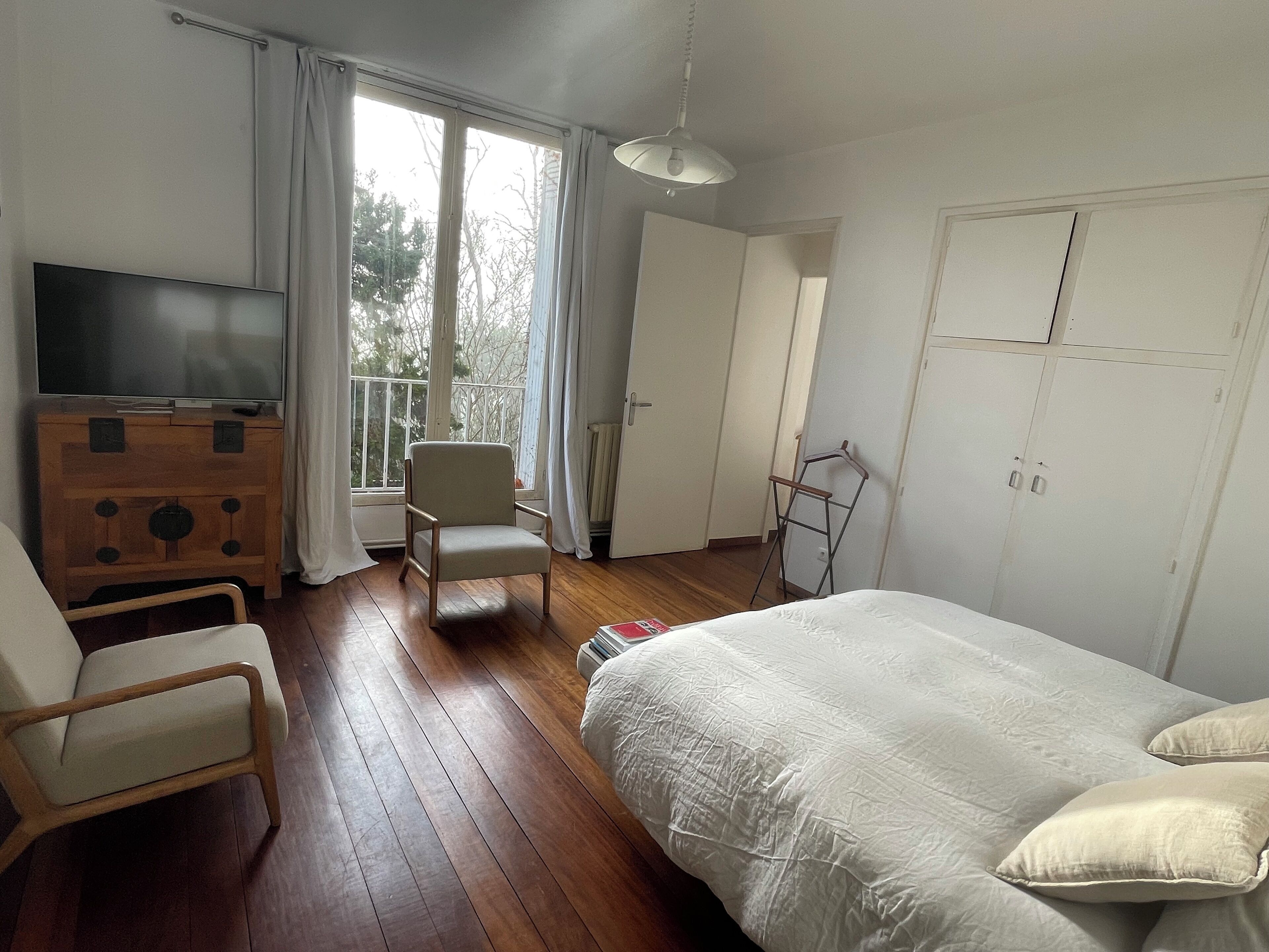 A bedroom with a bed, a chair, a TV, a dresser, and a window with curtains.