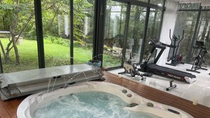 Un jacuzzi con cubierta de madera, una cinta de correr y equipo de ejercicio al fondo.