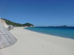 A beach with a clear blue sky, sandy shore, and a structure with a corrugated roof on the left.