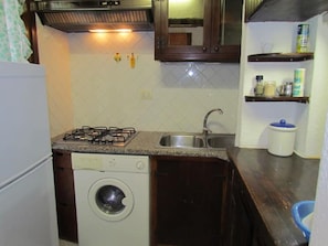 A compact kitchen with a gas stove, dishwasher, and washing machine. - Chalet the castle (Villasimius)
