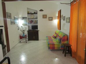 A living room with a colorful sofa, a small table, and a television on a stand. - Chalet the castle (Villasimius)