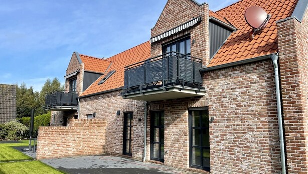 A two-story brick house with a red-tiled roof, a balcony with metal railings, and a paved driveway. - Vacation apartment Starboard Greetsiel (Greetsiel)