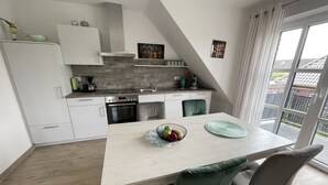 A modern kitchen with white cabinets, a dining table with chairs, and a large window with curtains. - Vacation apartment Starboard Greetsiel (Greetsiel)