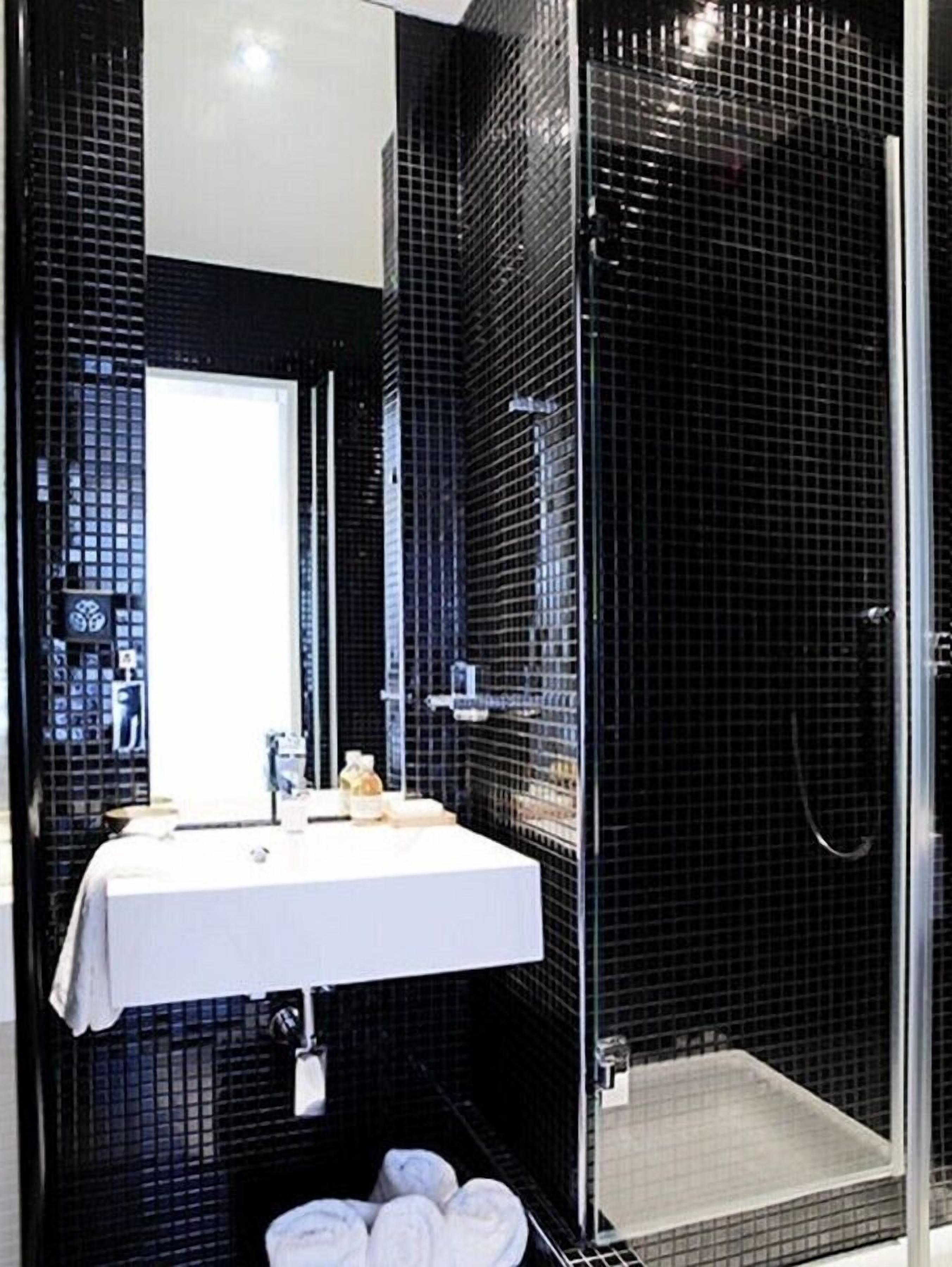 A modern bathroom with a white sink, a glass shower enclosure, and black tiled walls.