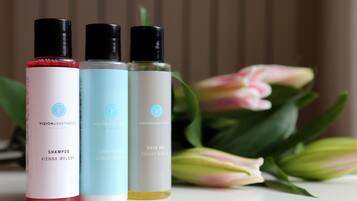 Drei Flaschen Shampoo, Conditioner und Duschgel vor floralem Hintergrund.