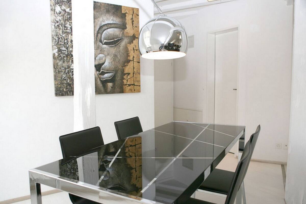 Une salle à manger moderne avec une table à plateau en verre, des chaises noires et un luminaire suspendu.