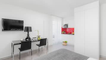 Una habitación de hotel moderna con televisión de pantalla plana, un escritorio con dos sillas, una pequeña cocina con microondas y un ventanal grande.