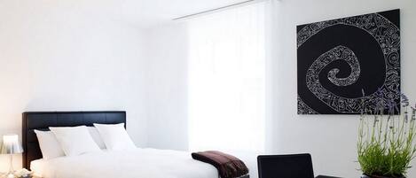 Un dormitorio moderno con cama, mesita de noche, lámpara y una obra de arte en la pared.
