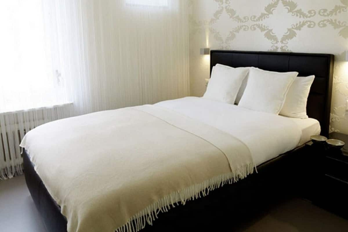 Un lit bien fait, avec du linge de lit blanc et une tête de lit sombre, dans une chambre d’hôtel.