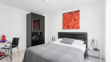 Ein modernes Hotelzimmer mit einem großen Bett, einem Schreibtisch und einem Sessel. An der Wand hängt ein Gemälde von roten Blumen.