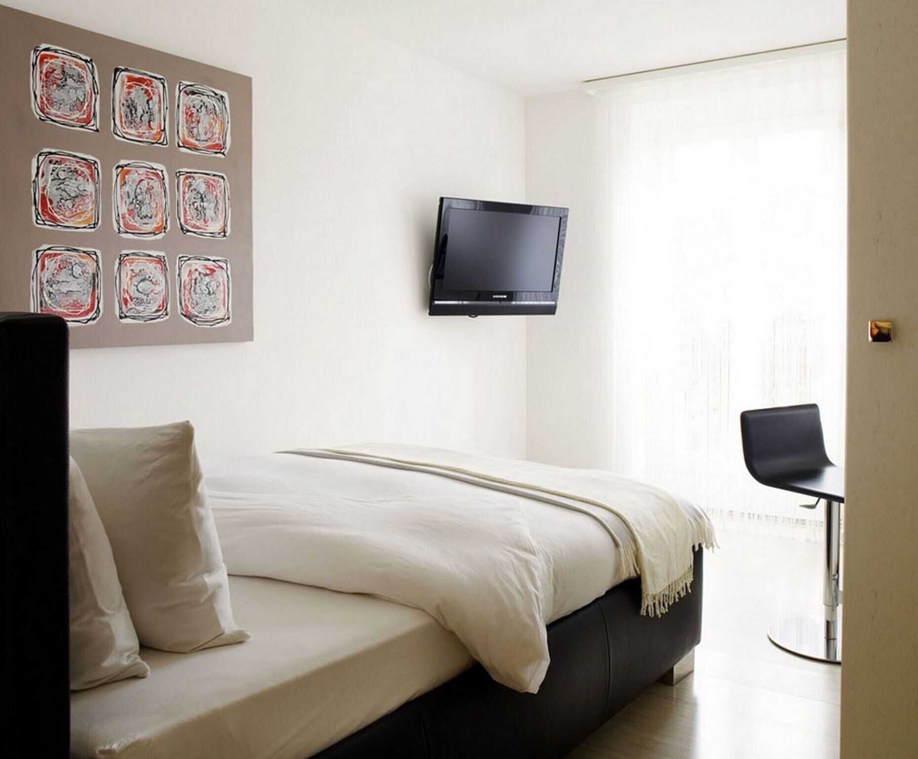 A bedroom with a bed, a TV mounted on the wall, and a window.