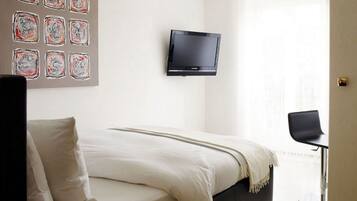 Ein Schlafzimmer mit einem Bett, einem an der Wand montierten Fernseher und einem Fenster.