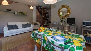 A dining area with a table set for four, a white sofa, a bookshelf, and a television in the background. - Villa with pool in the green (Lucca)