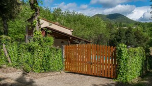 A rustic house with a wooden fence, surrounded by lush greenery and mountains in the background. - Villa with pool in the green (Lucca)