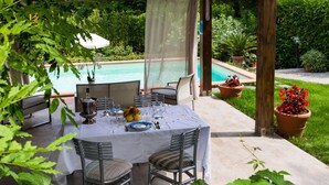 An outdoor patio with a table set for dining, surrounded by lush greenery and a pool. - Villa with pool in the green (Lucca)