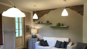A modern living room with a white sofa, two pendant lights, a small side table with a lamp, and a brick accent wall. - Villa with pool in the green (Lucca)