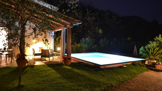 A well-lit outdoor pool area with a pergola, seating, and potted plants. - Villa with pool in the green (Lucca)