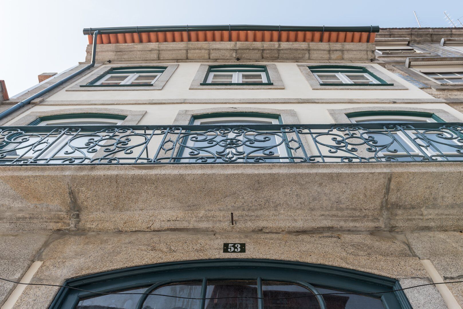 A building with a stone facade, green window frames, and a decorative metal railing.