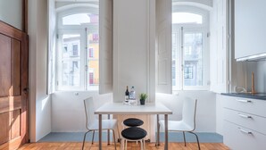 A modern kitchen with a wooden floor, white cabinetry, and a dining area with two chairs. - GuestReady - Clerigos-Virtudes Apartments (Porto)