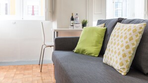 A living room with a grey sofa, a green pillow, and a patterned pillow. A chair is visible in the foreground. - GuestReady - Clerigos-Virtudes Apartments (Porto)