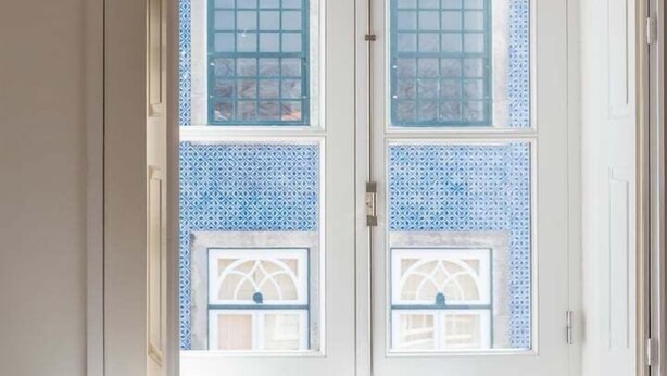 A doorway with a woven light fixture and a view of a building with blue patterned windows. - GuestReady - Clerigos-Virtudes Apartments (Porto)