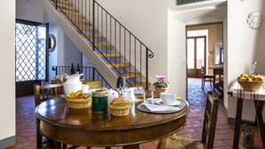 A dining area with a wooden table set for breakfast, a staircase, and a view of the kitchen in the background. - The Chapel - ancient little country church (GRASSINA)