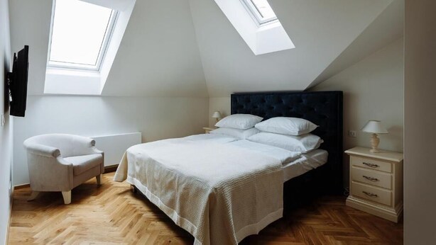 A bedroom with a bed, two bedside tables, a chair, and two skylights. - Elegant Suite 4 (Hlavní město Praha)