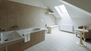 A modern bathroom with a skylight, a bathtub, a sink, and a toilet. - Elegant Suite 4 (Hlavní město Praha)