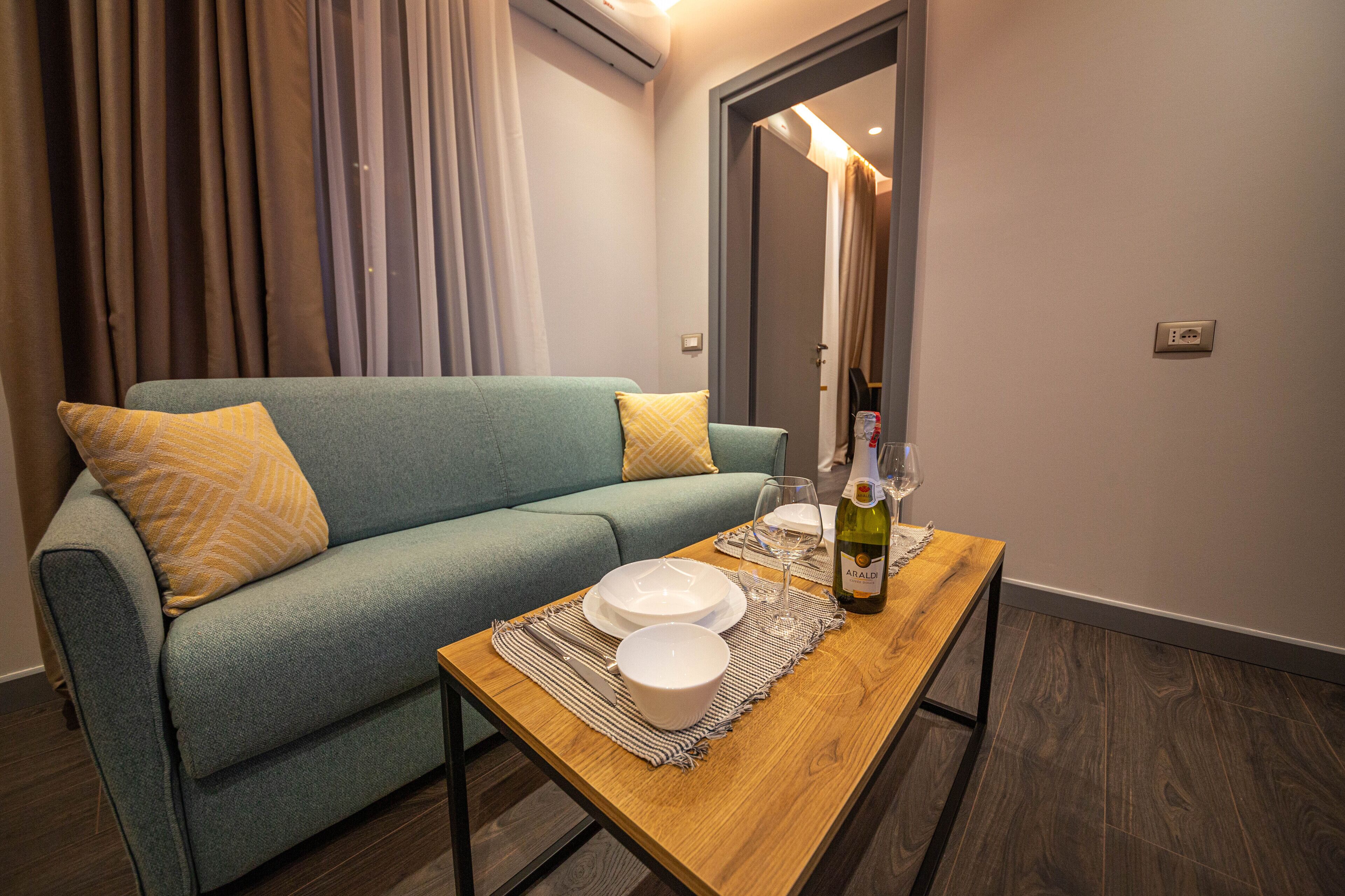 Una sala de estar moderna con un sofá azul verdoso, una mesa de centro de madera y una botella de vino.