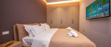 Una cama bien hecha con sábanas blancas, una mesita de noche de madera y un cuadro con una playa en la pared.
