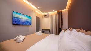 A modern hotel room with a large bed, a flat-screen TV mounted on the wall, and a view of a landscape through the window. - Blloku Unique Apartments (Tirana)