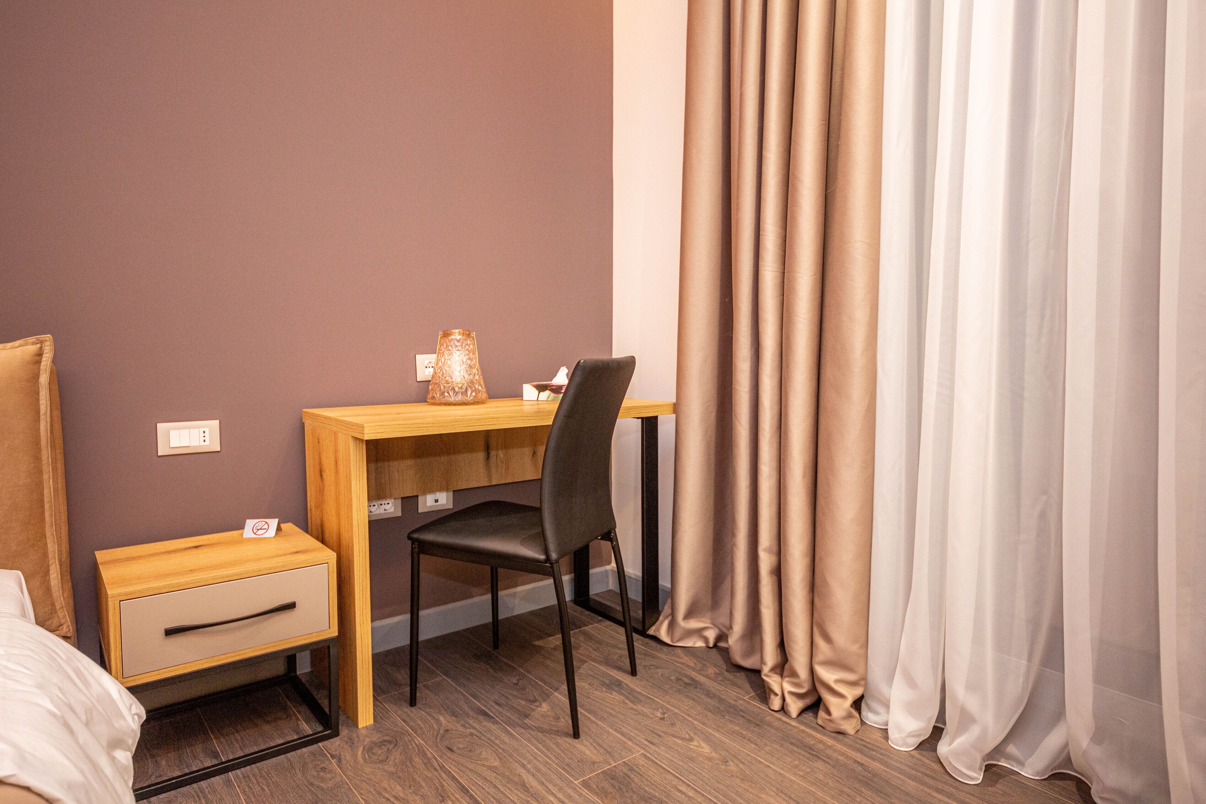 Una habitación de hotel con un escritorio de madera, una silla, una mesita de noche con cajón y una cama.