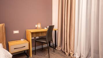 Una habitación de hotel con un escritorio de madera, una silla, una mesita de noche con cajón y una cama.