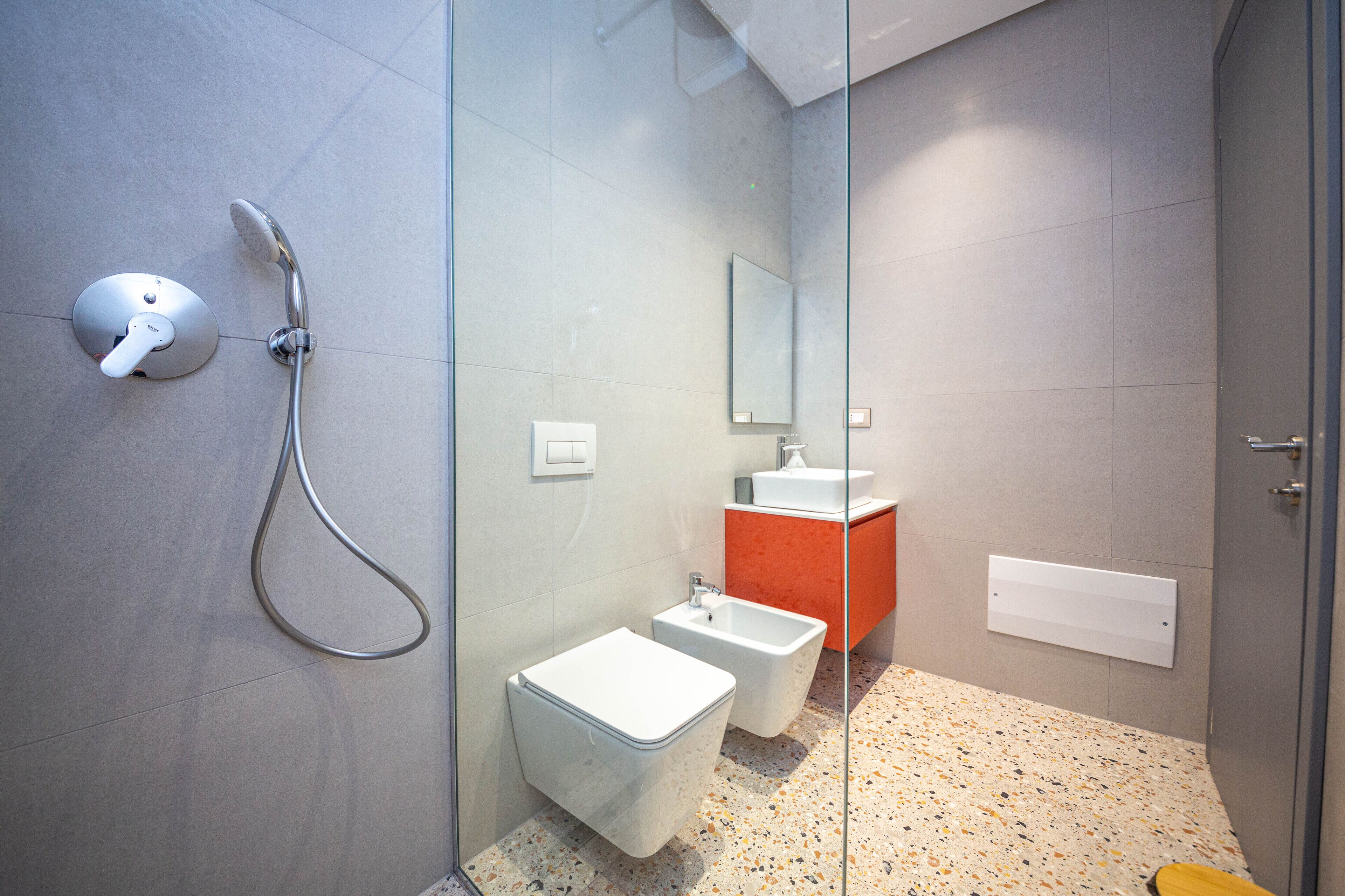 Une salle de bain moderne avec une douche à parois de verre, des toilettes blanches et un lavabo devant un mur d’accent rouge.