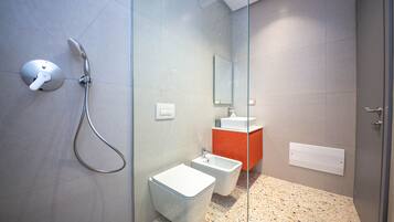 Une salle de bain moderne avec une douche à parois de verre, des toilettes blanches et un lavabo devant un mur d’accent rouge.