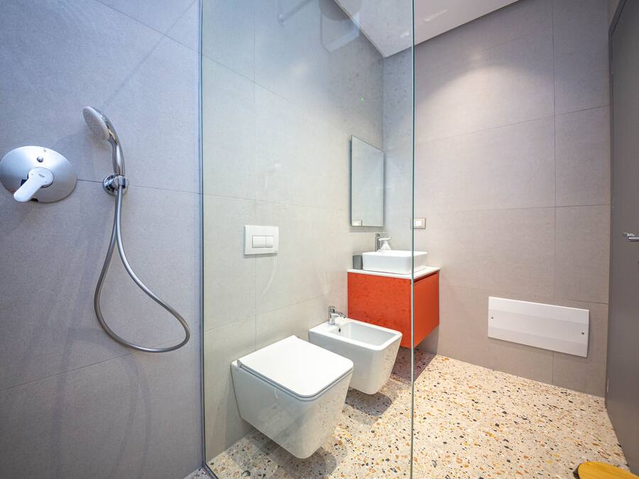 Une salle de bain moderne avec une douche à parois de verre, des toilettes blanches et un lavabo devant un mur d’accent rouge.