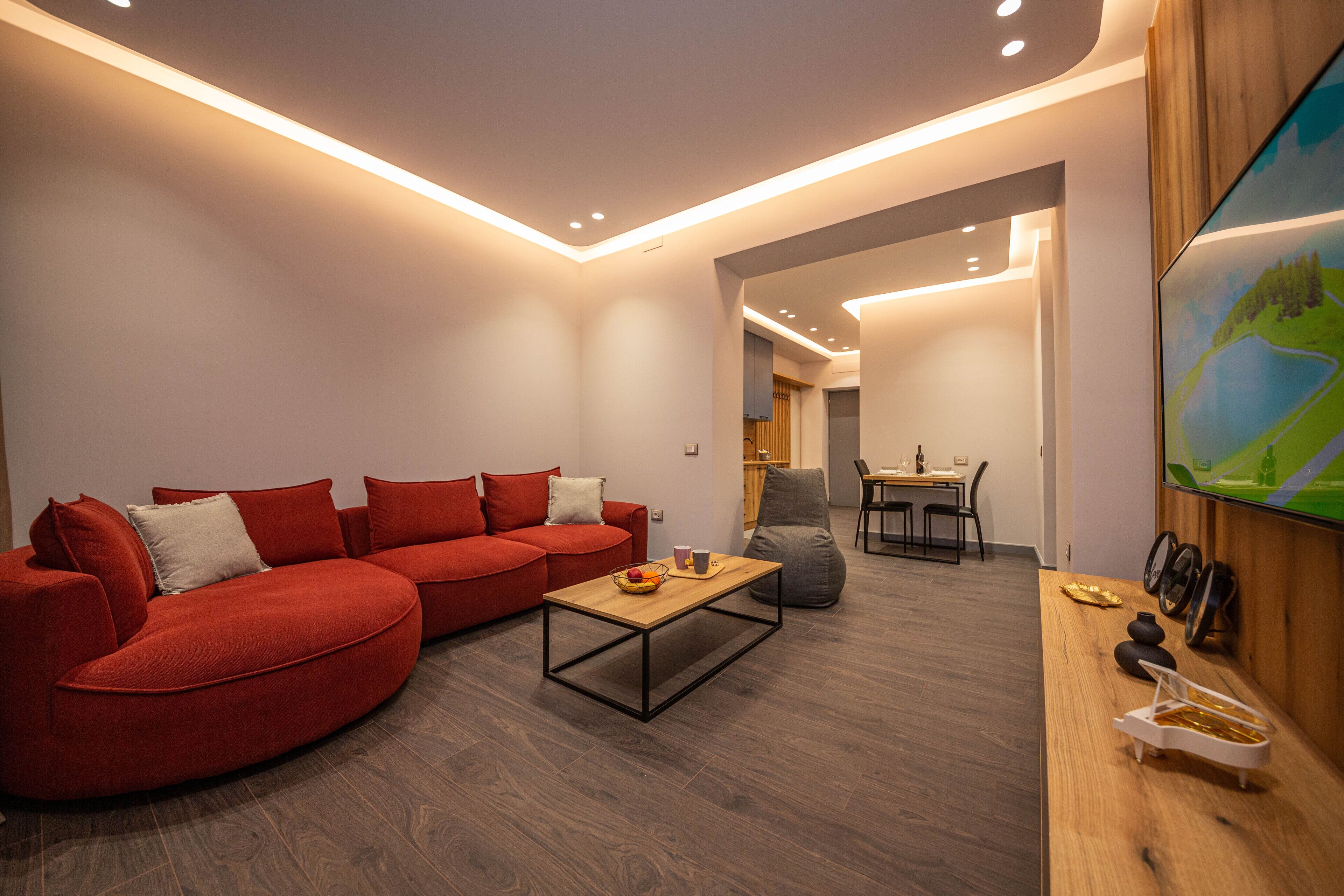 A modern living room with a red sofa, a wooden coffee table, and a TV mounted on the wall.