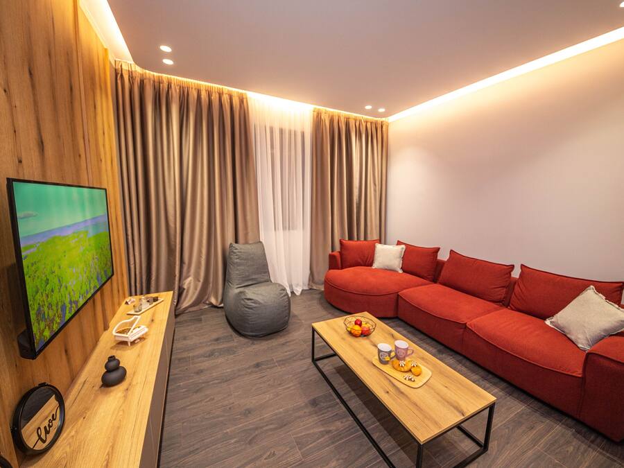 Ein modernes Wohnzimmer mit einem roten Sofa, einem Holztisch, einem grauen Sitzsack und einem Fernseher an der Wand.