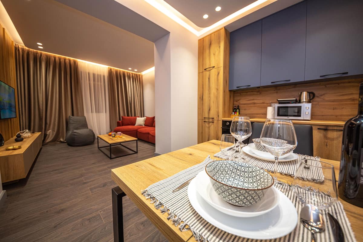 A modern living room with a wooden dining table set for two, a red sofa, and a kitchen area with a microwave and kettle.