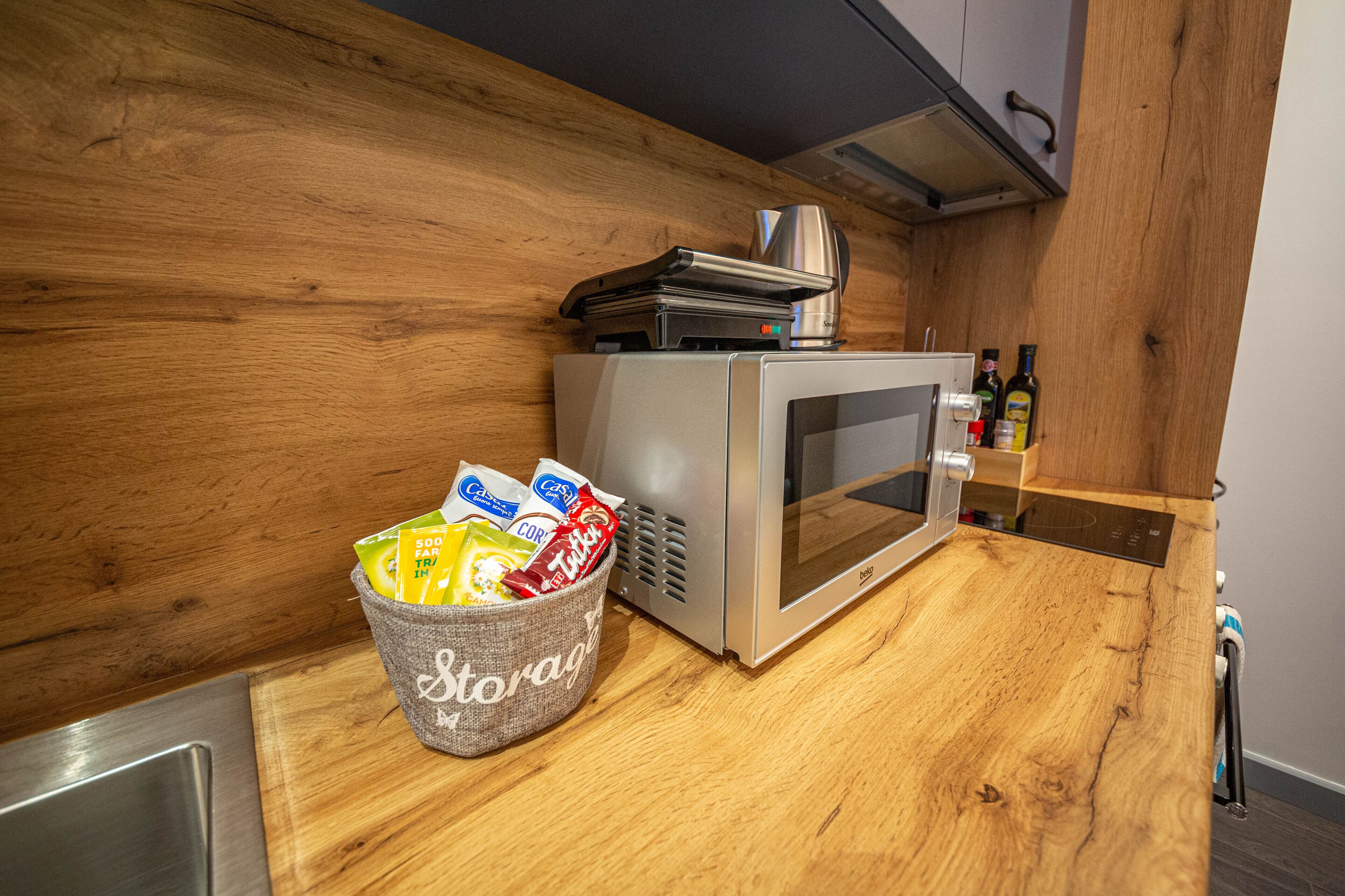 Una cocina con microondas, cafetera y una cesta con aperitivos, etiquetada como 'Storage'.