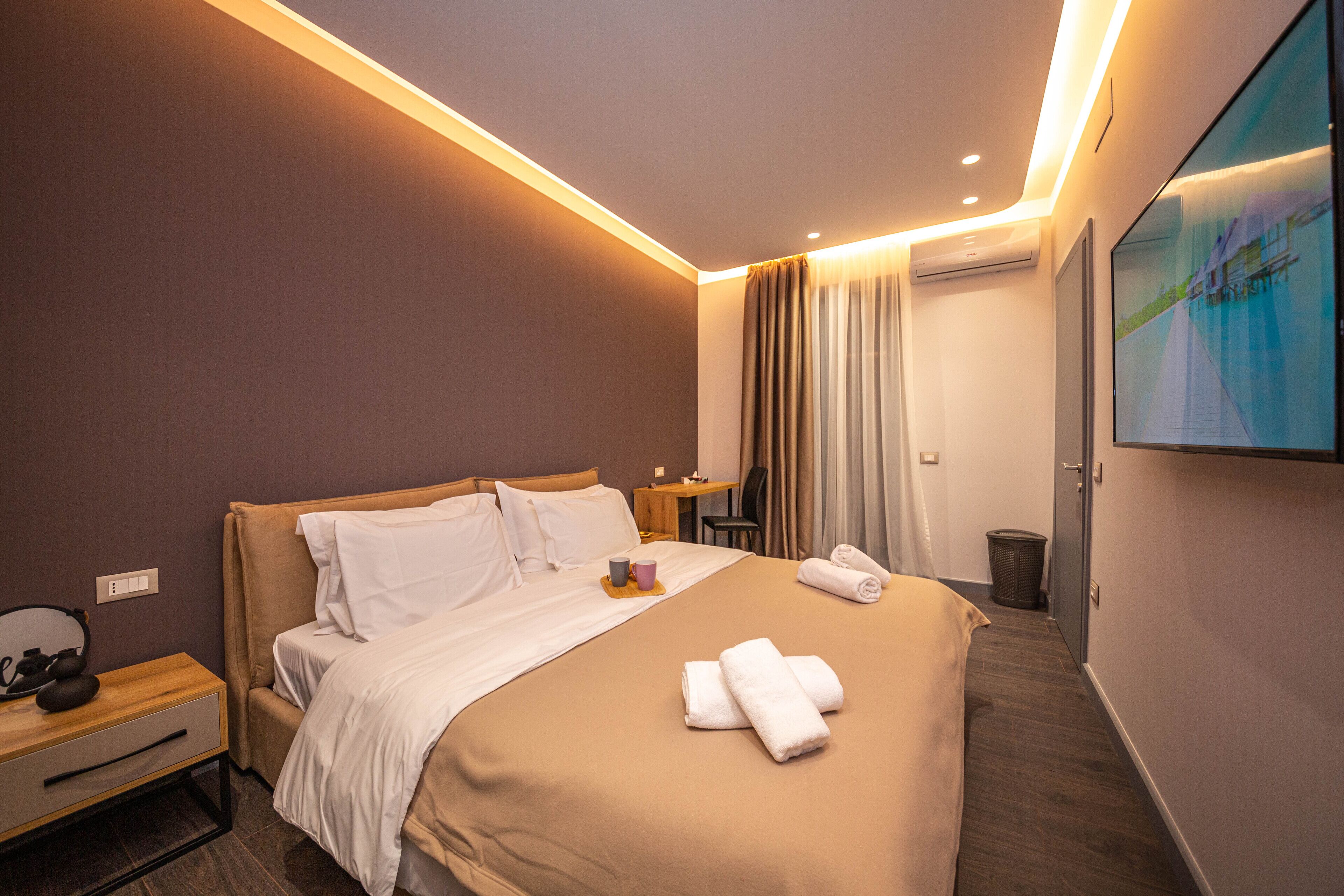 A modern hotel room with a large bed, a desk, a chair, and a TV mounted on the wall.