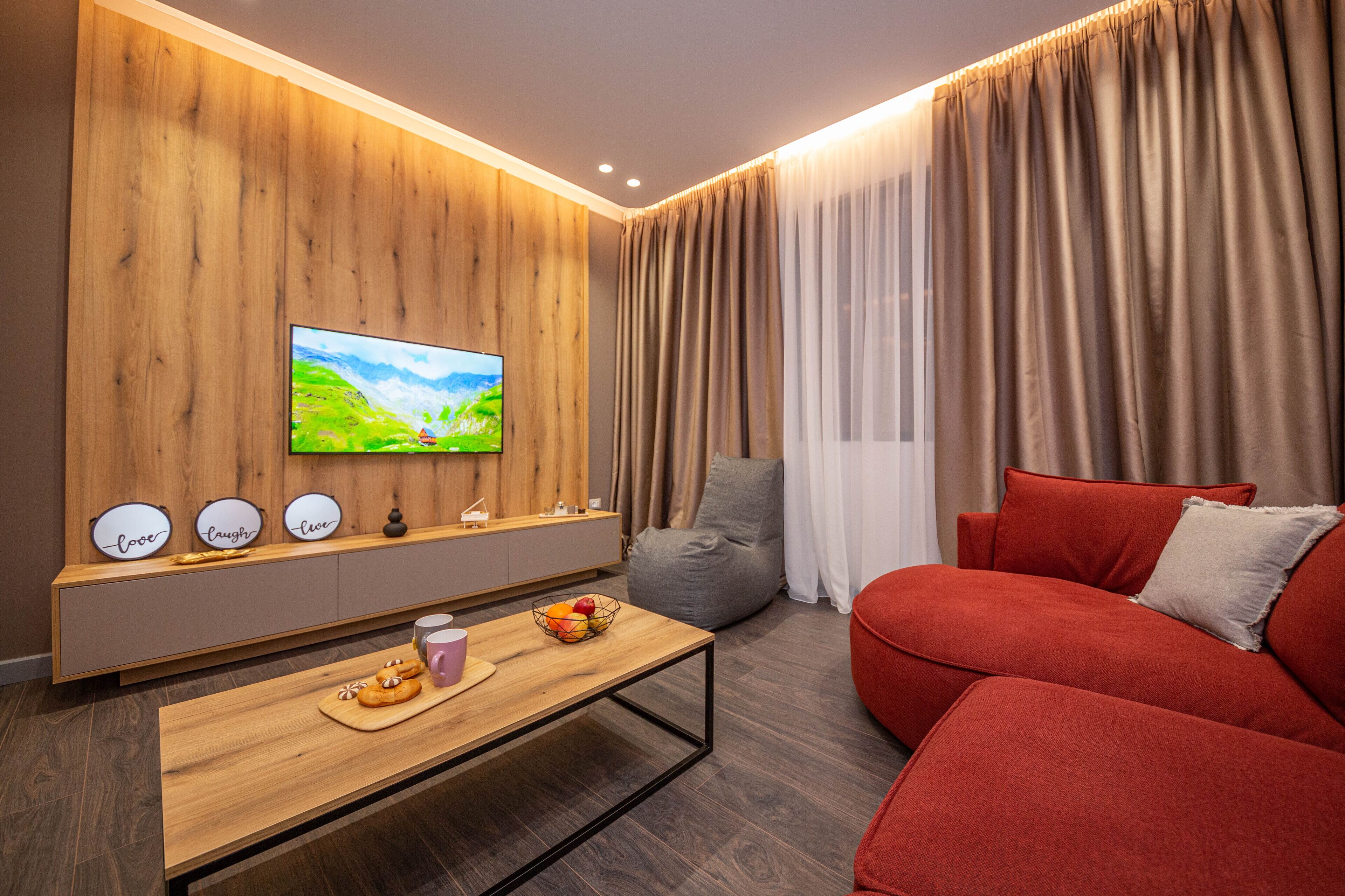 Una sala de estar moderna con una pared de acento de madera, un televisor de pantalla plana, un sofá rojo, una mesa de centro con aperitivos y un asiento informal de forma de saco gris.