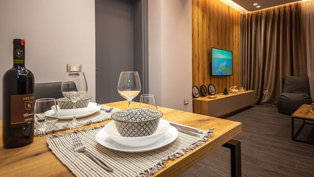 A dining area with a wooden table set for two, a bottle of wine, and a bowl with a patterned design. - Blloku Unique Apartments (Tirana)