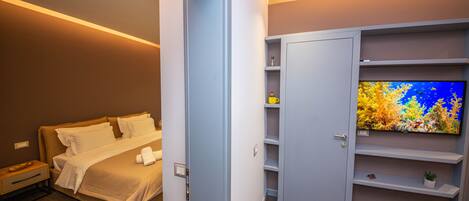 A modern hotel room with a bed, a TV, a wardrobe, and a small table with a glass.