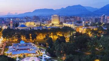 A cityscape at dusk with illuminated buildings, a prominent dome structure, and mountains in the background.