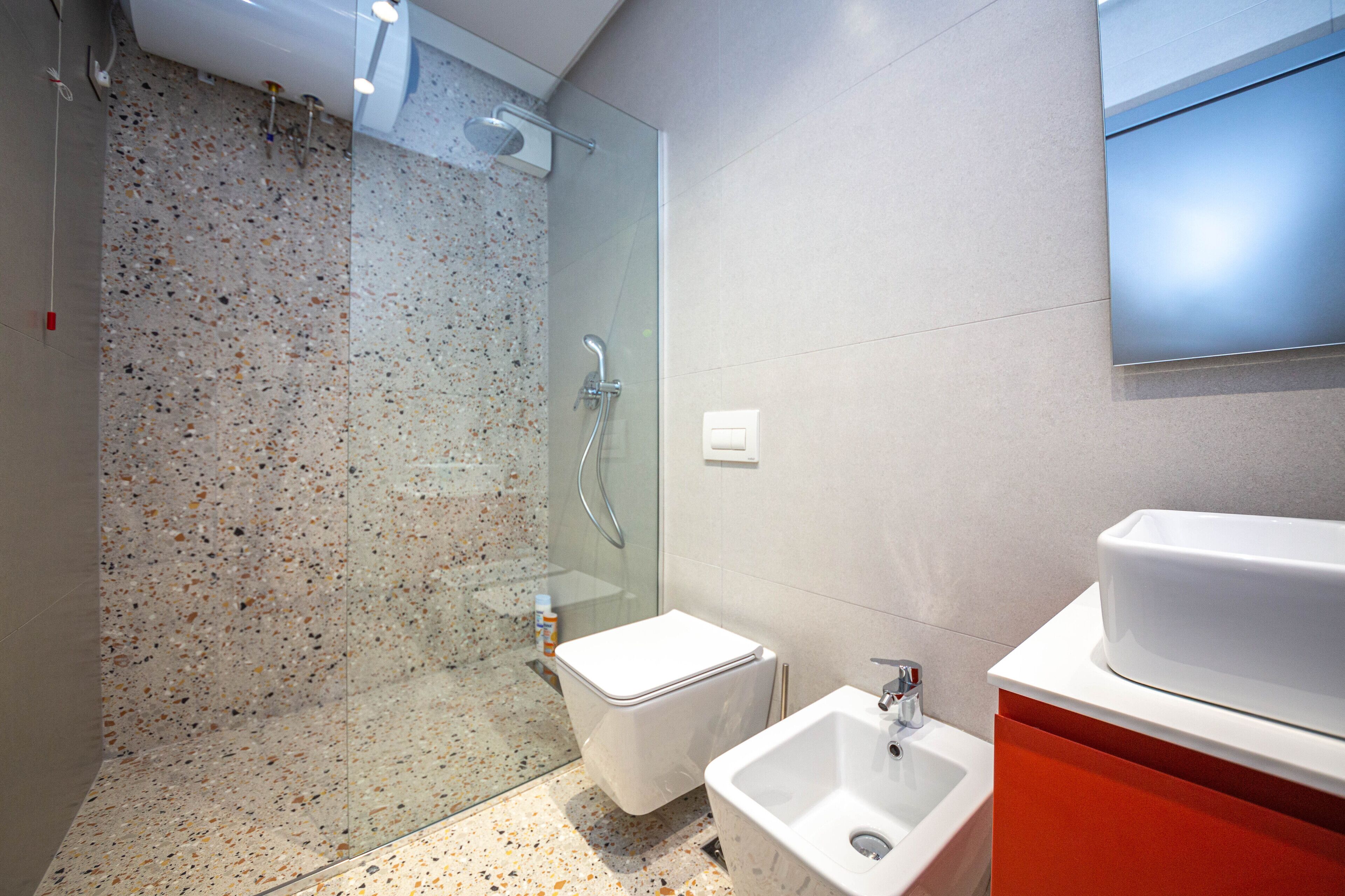 Ein modernes Badezimmer mit Duschkabine aus Glas, einer weißen Toilette und einem Waschbecken mit rotem Unterschrank.
