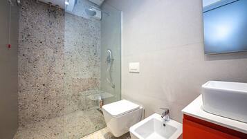 Ein modernes Badezimmer mit Duschkabine aus Glas, einer weißen Toilette und einem Waschbecken mit rotem Unterschrank.