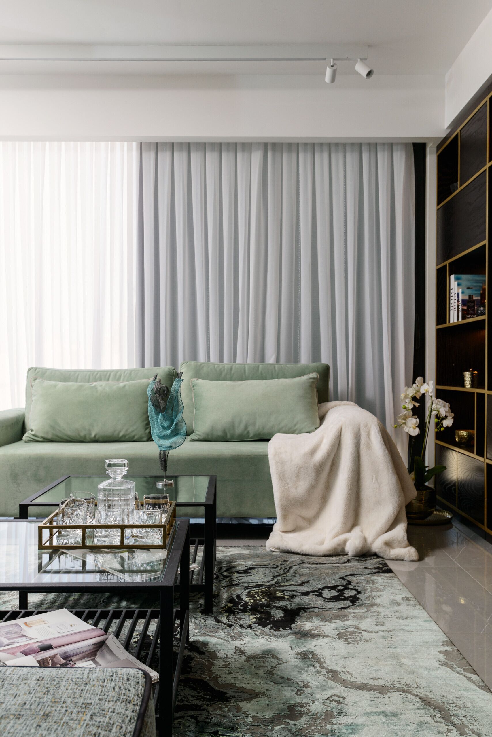 A modern living room with a green sofa, a glass coffee table, and a patterned rug.