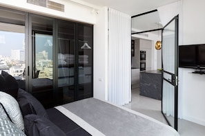 A modern bedroom with a large bed, a sliding glass door to a balcony, and a view of the cityscape.