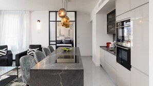 A modern kitchen with a central island, built-in oven, and a dining area with chairs and a table. - MAMAD High End 2BR with City & Sea View by FeelHome (Tel Aviv - Jaffa)